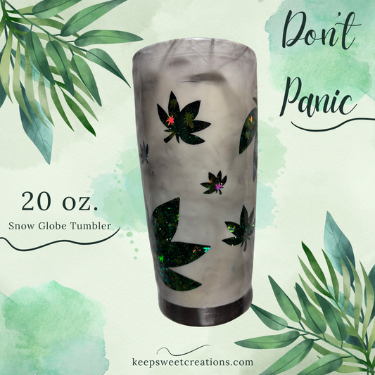 A 20 oz. white snow globe tumbler with a frosted finish and green leaf patterns, containing floating glitter, displayed with a 'Don't Panic' text and website credit to keepsweetcreations.
