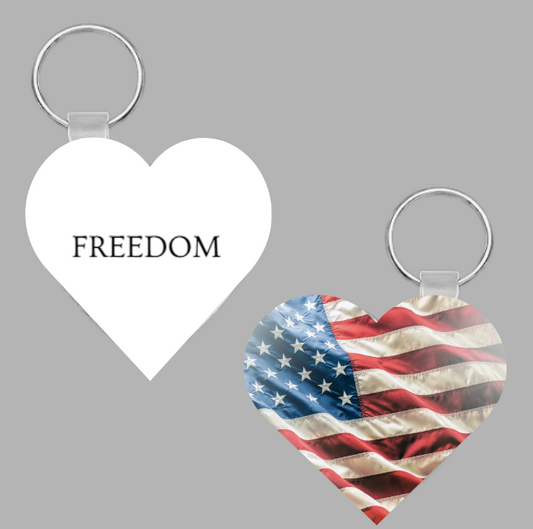 Double-sided heart-shaped FREEDOM keychain. One side displays the word FREEDOM in bold black text, the other side features a waving American flag design. Patriotic fundraiser by Keep Sweet Creations supporting Turning Point USA.