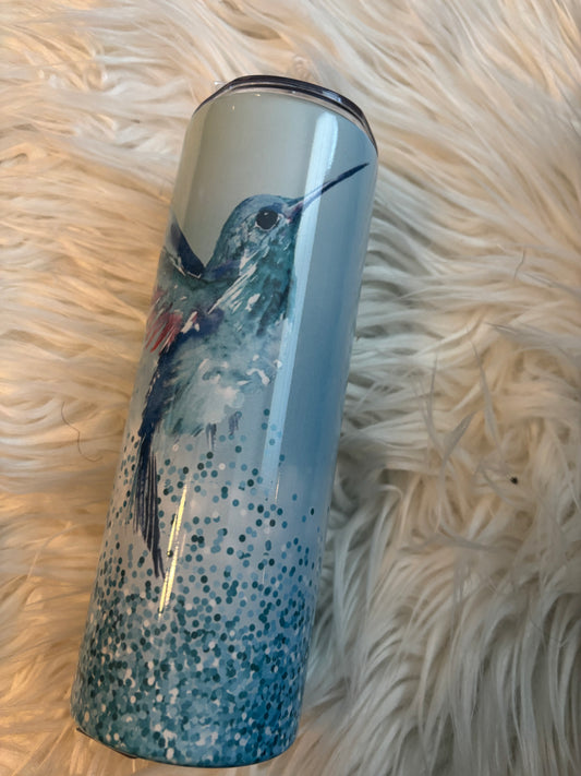 20 oz stainless steel tumbler with blue sparkles and a hummingbird design on a white faux fur background