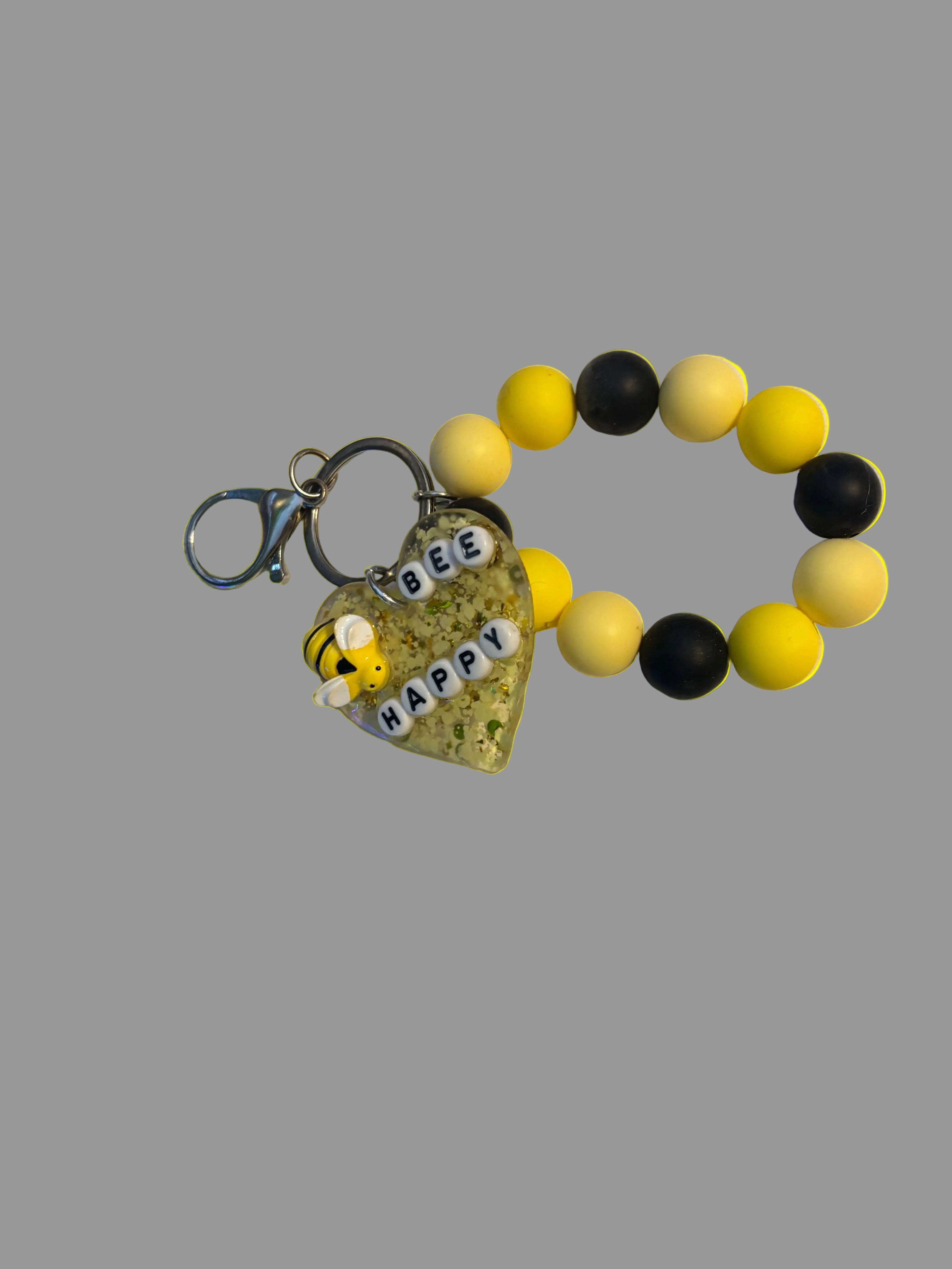 Yellow and black beaded keychain with a bee charm on a textured surface.