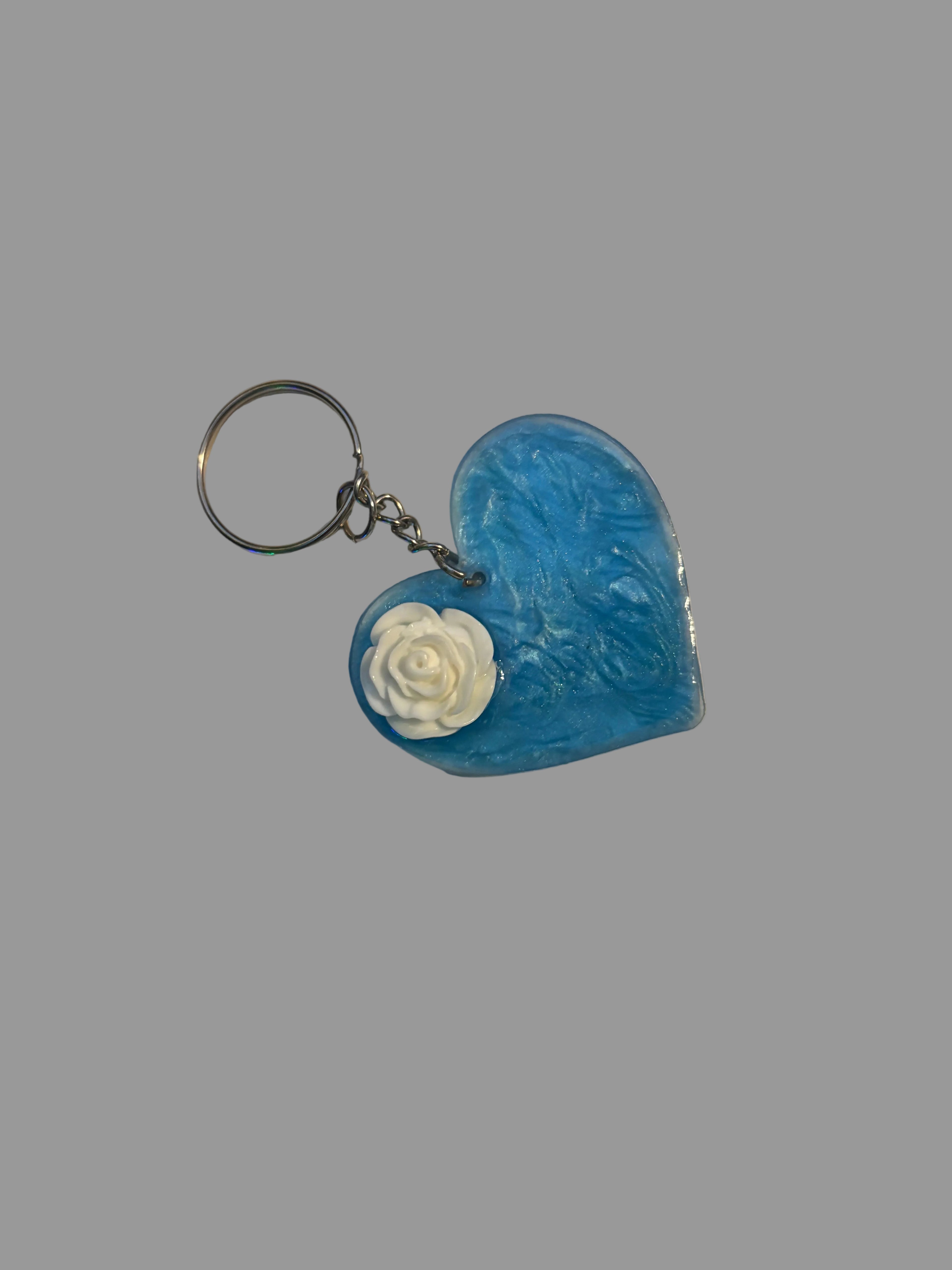 Blue heart-shaped keychain with a white rose on a textured surface