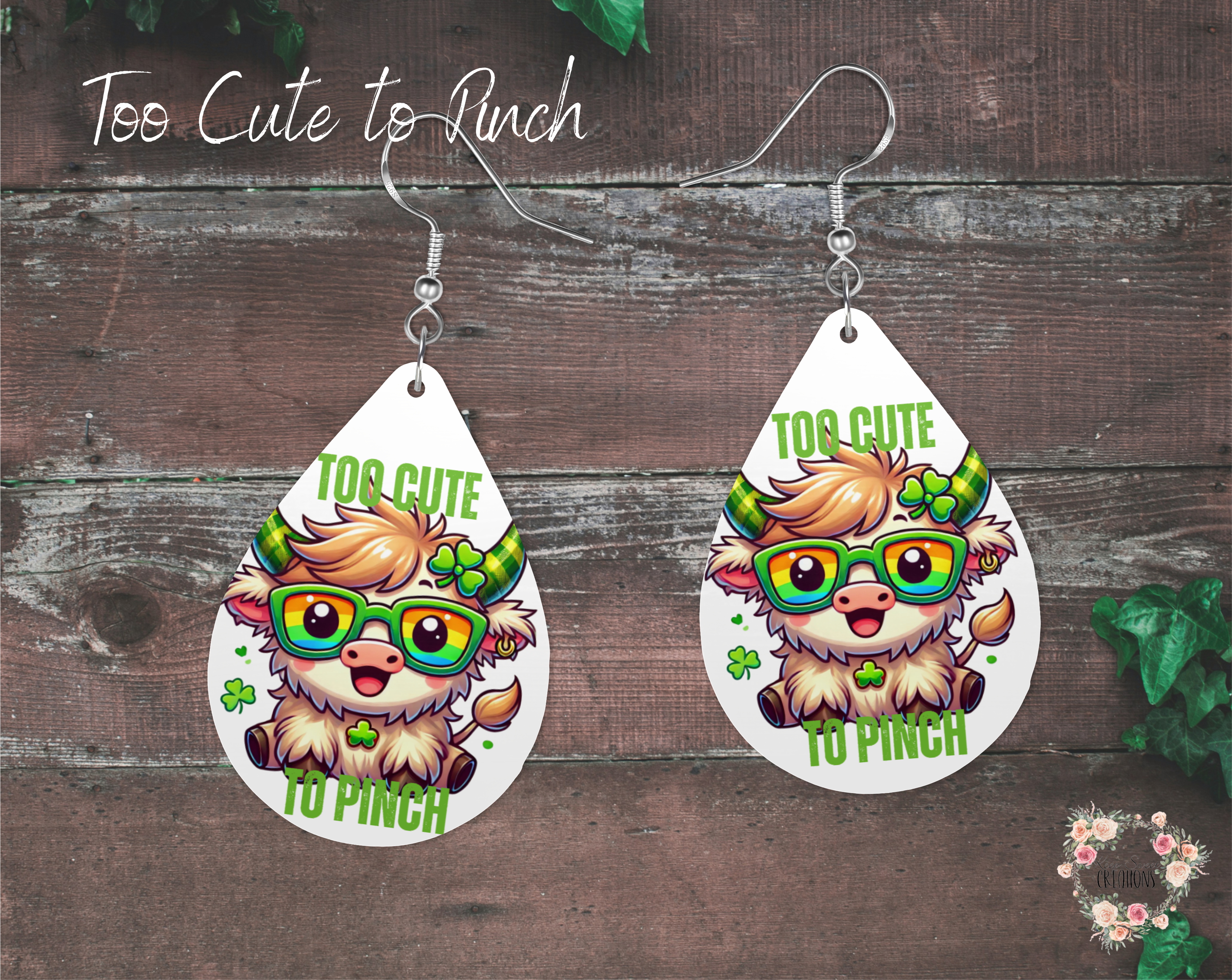 "A pair of teardrop-shaped St. Patrick’s Day earrings featuring an adorable white Highland cow wearing rainbow glasses and a shamrock headband. The cow is surrounded by green shamrocks with the phrase 'Too Cute to Pinch' in bold green text. These lightweight sublimation wood earrings have nickel-free hypoallergenic hooks, making them a fun and festive accessory."